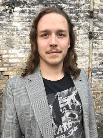 A portrait photo of Jan Nash in a chequered jacket in front of a brick wall